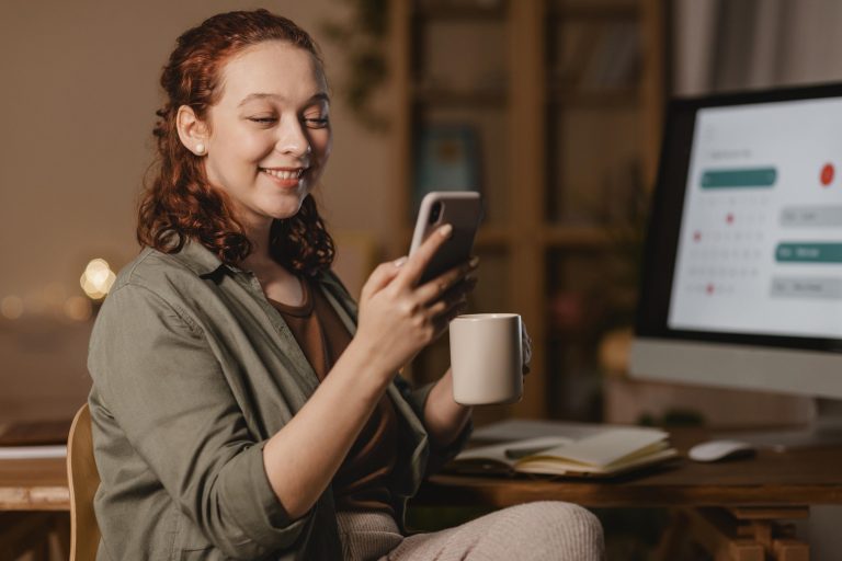 mulher-em-casa-usando-smartphone-na-frente-do-computador-enquanto-toma-cafe
