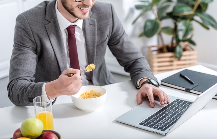 businessman working on laptop while eating breakfast at kitchen